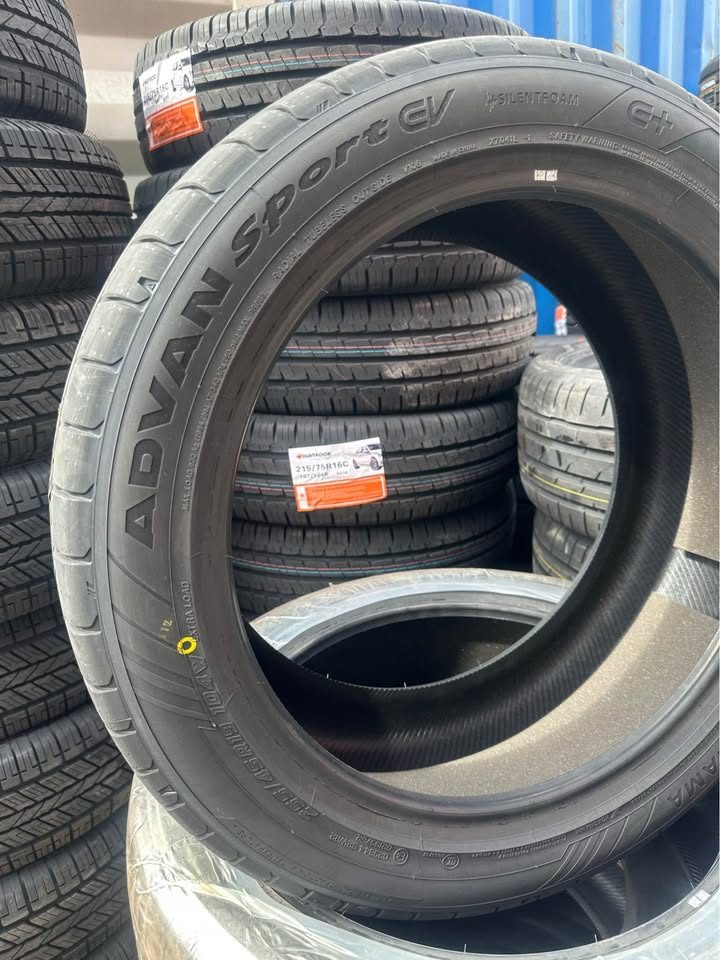 Stack of tires with 'Advan Sport CV' branding in a warehouse setting.
