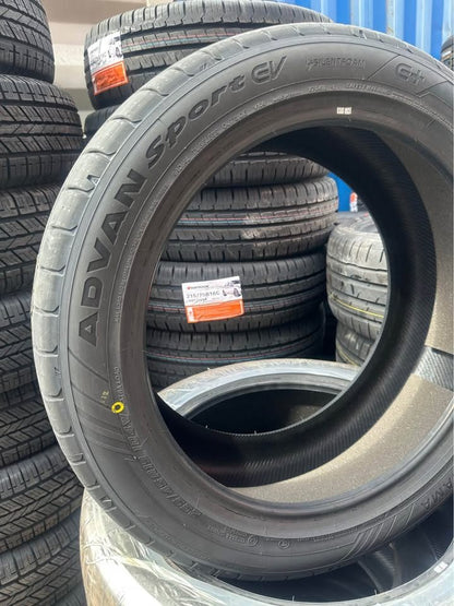 Stack of tires with 'Advan Sport CV' branding in a warehouse setting.