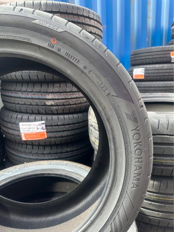 Yokohama tire with other tires stacked in the background against a blue wall.