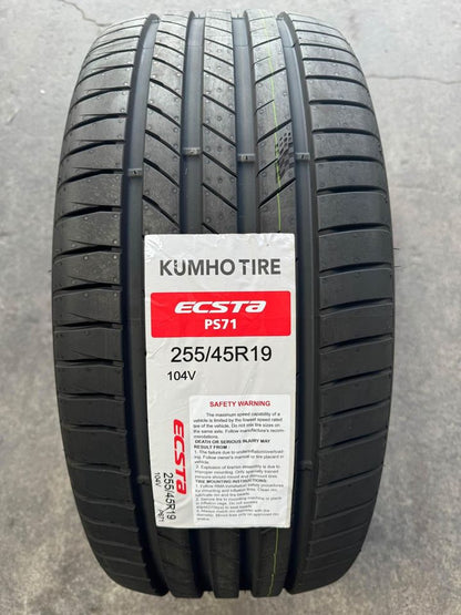 A black KUMHO ECSTA PS71 tire positioned upright, featuring product labels and tread pattern visible.